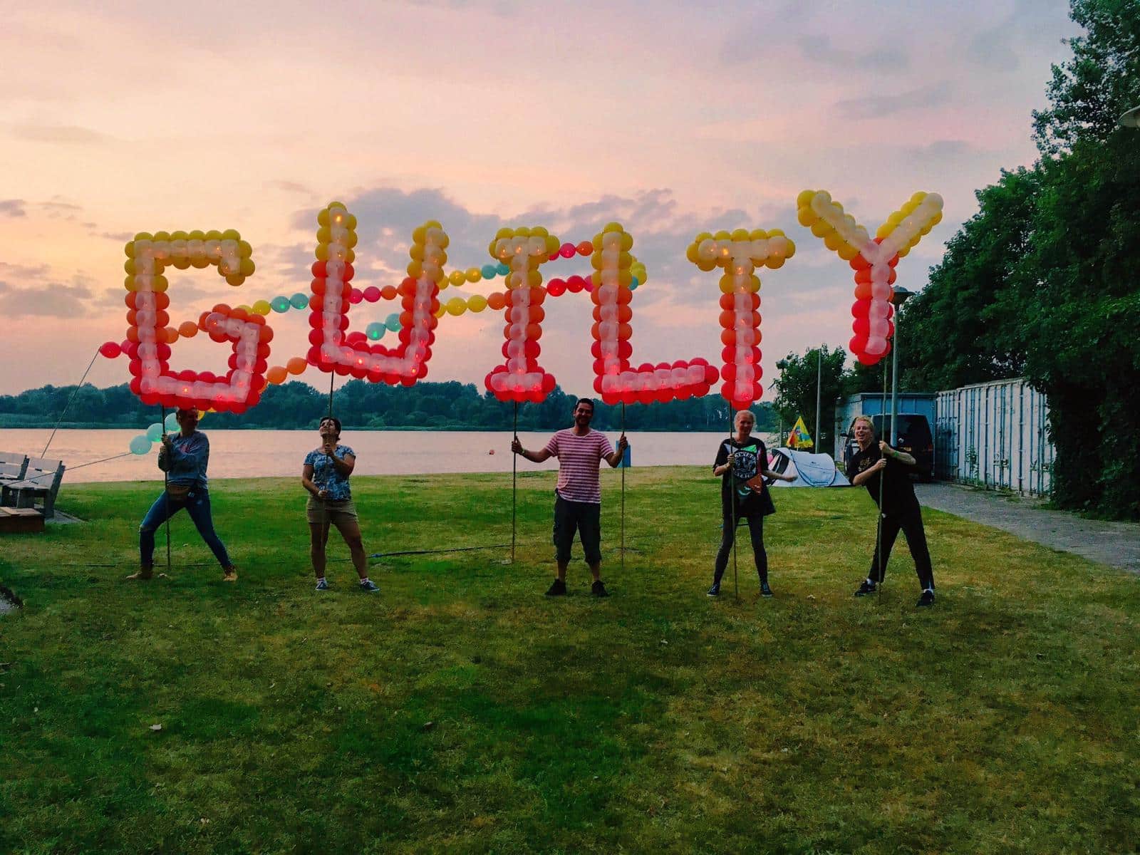 Crew carrying Spellbound balloon letters at golden-hour sunset by the waterside at Guilty Pleasure Festival in Amsterdam (2019) — Spellbound — High Lines