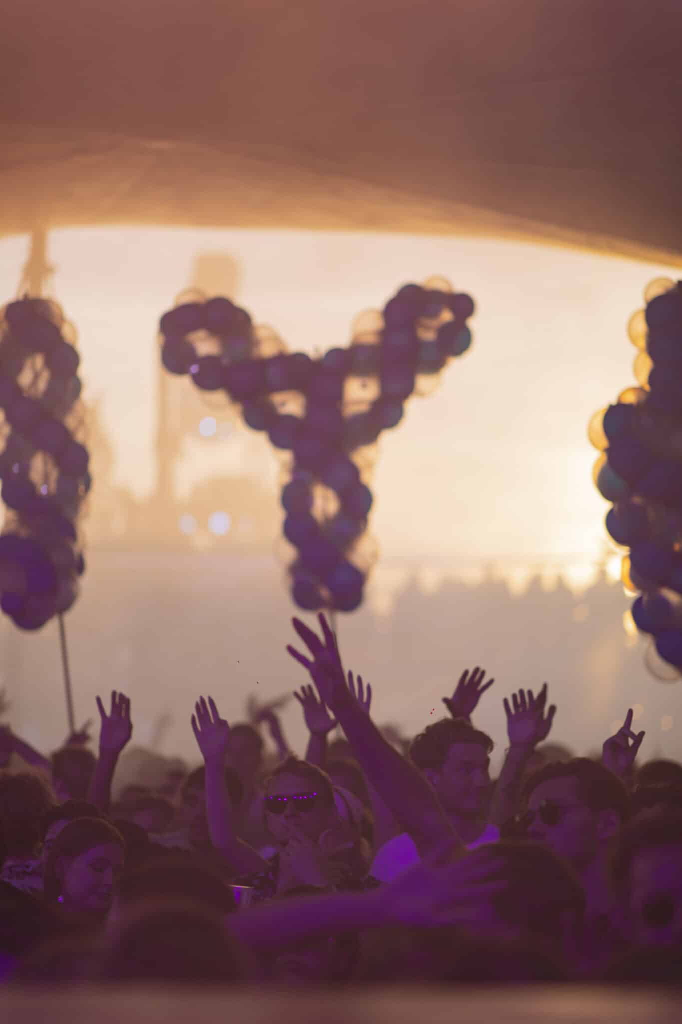 Spellbound balloon letters silhouetted against golden sunset with hands raised at Thuishaven Amsterdam for DJ Colyn — Out of Thin Air — Photo by Rachel Ecclestone